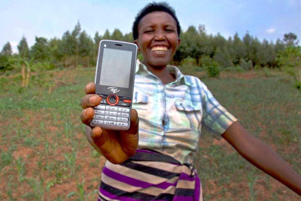 A smiling woman holds out her flip mobile phone.