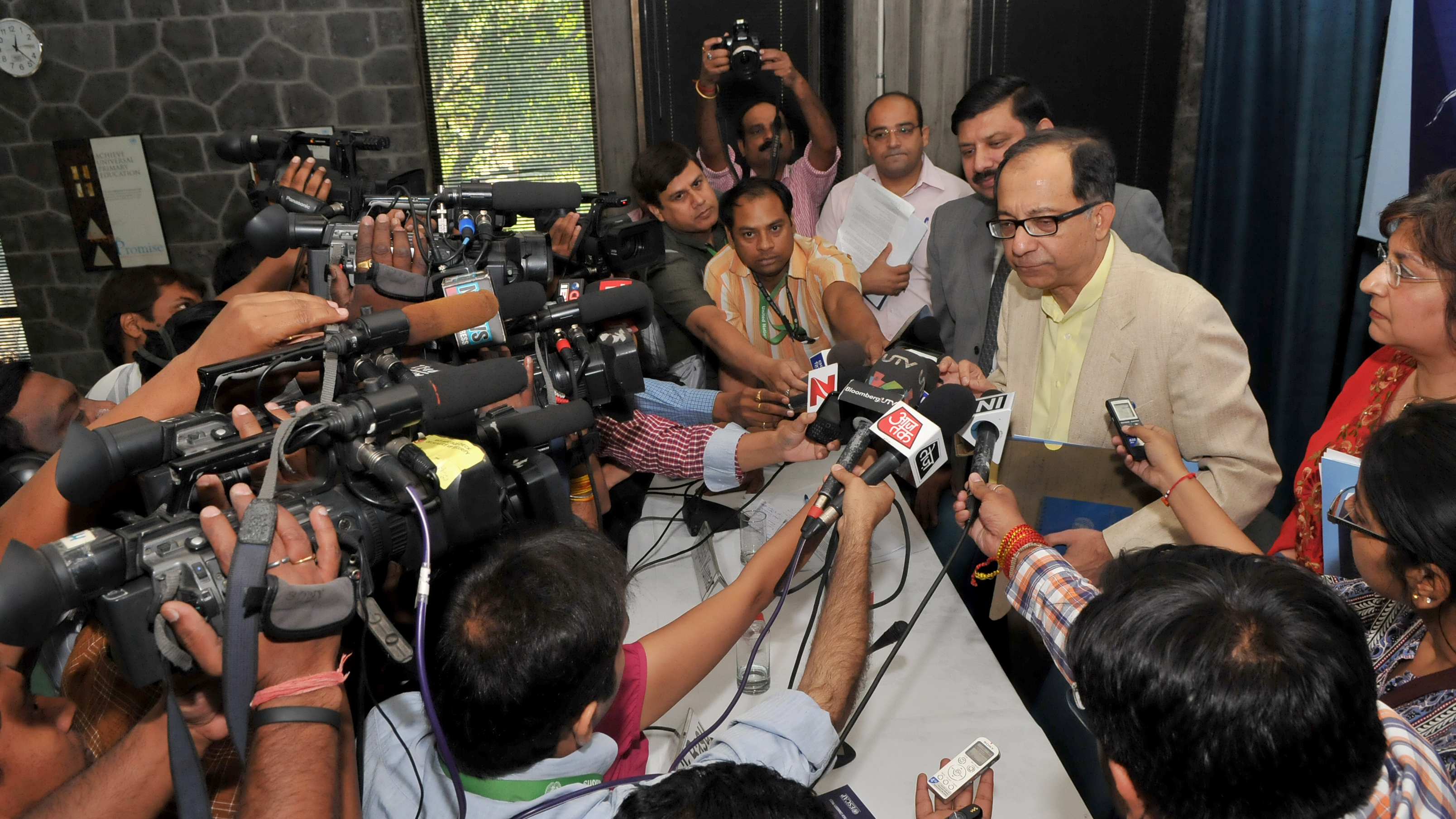 A group of people surround a man holding out microphones at him