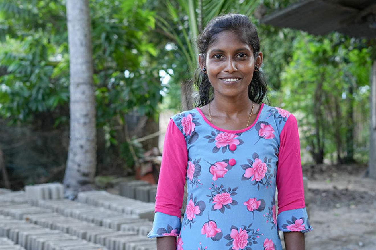 Une jeune femme sourit à la caméra. Derrière elle, des blocs de ciment empilés.