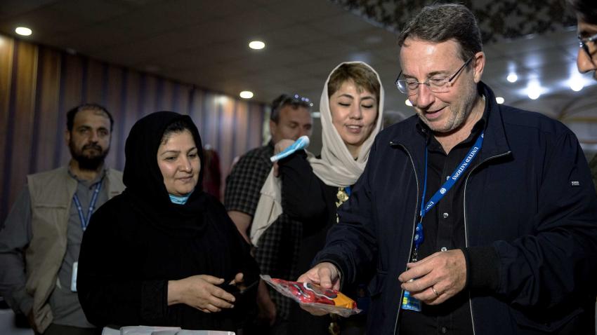 Achim looks at food with men and women standing next to him. The women wear veils.