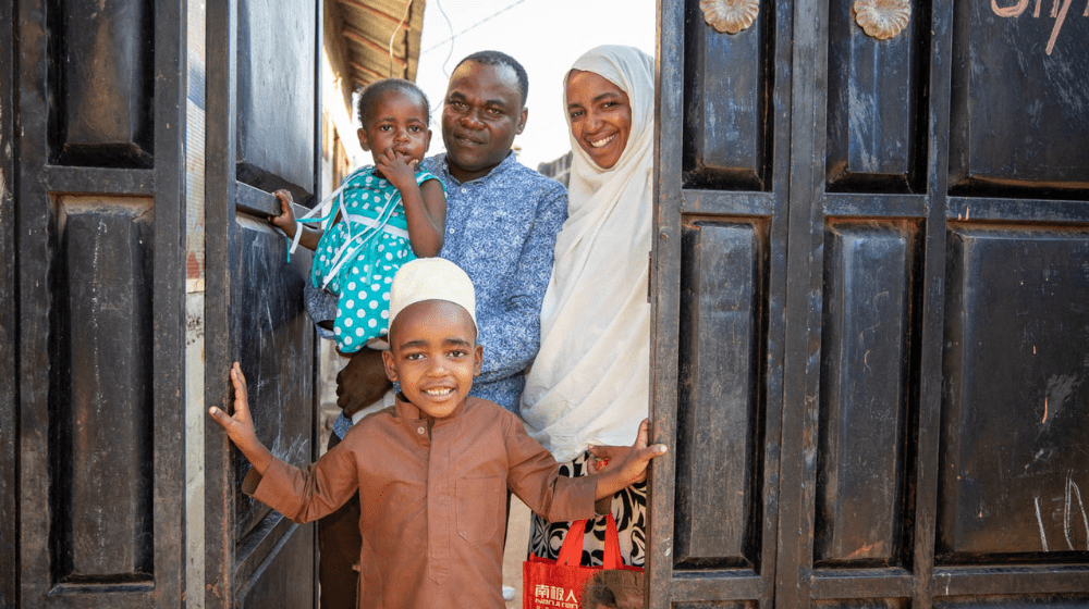 A smiling family of four stands in a doorway.