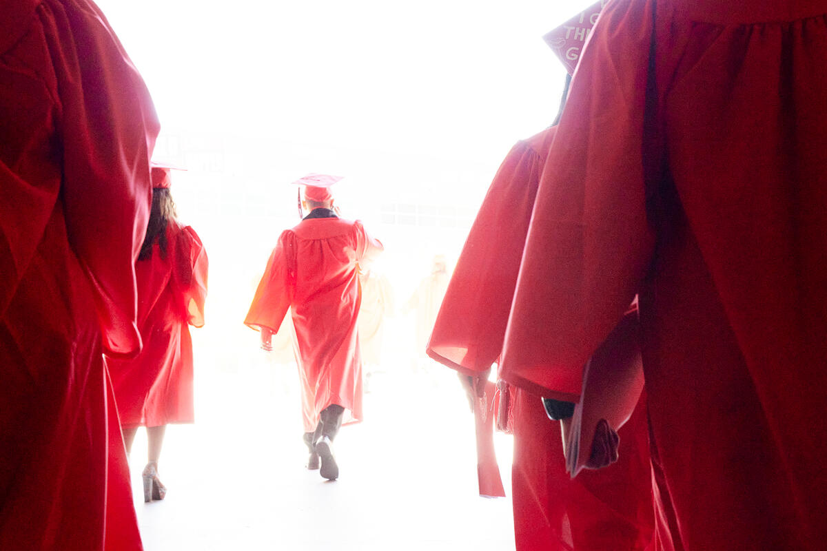 Students in cap and gown walking toward light