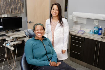 woman in dentist coat standing behind seated patient in exam room