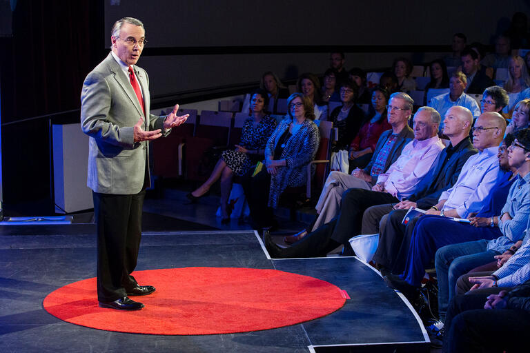 older man speaking in front of audience