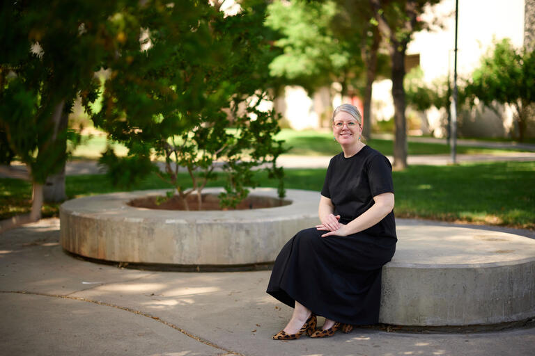 woman in black dress sits outside on round stone bench