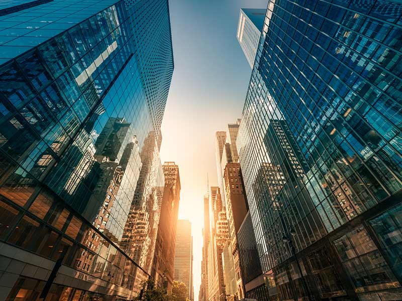 City skyline reflected on buildings lining a street with a setting sun