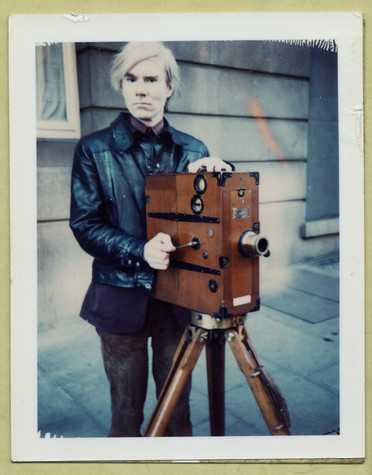 Andy Warhol poses outdoors with a silent film camera.