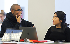 Two students work together over laptops on a table top